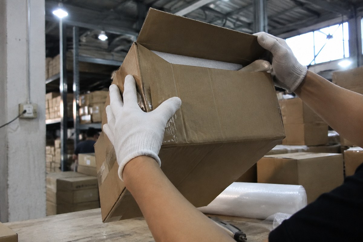 Gloved hands measuring the inside of an open carton with a tape measure