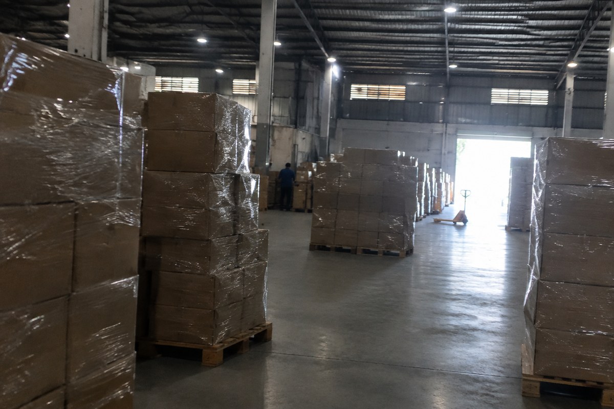 Gloved hands lifting a sealed carton from warehouse shelving beside stacked boxes